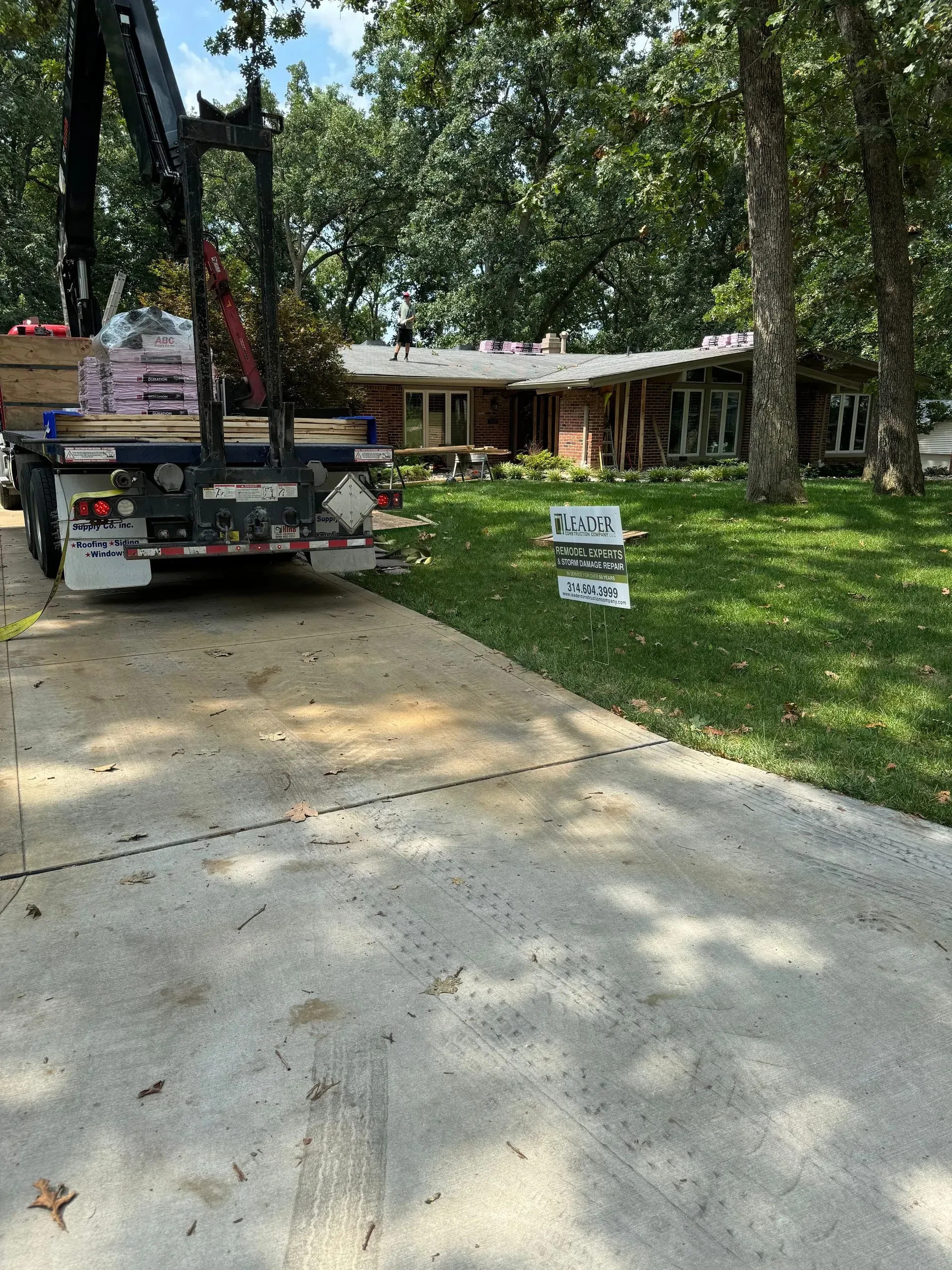 Driveway with a parked truck, yard signs, and a brick house among trees and green grass