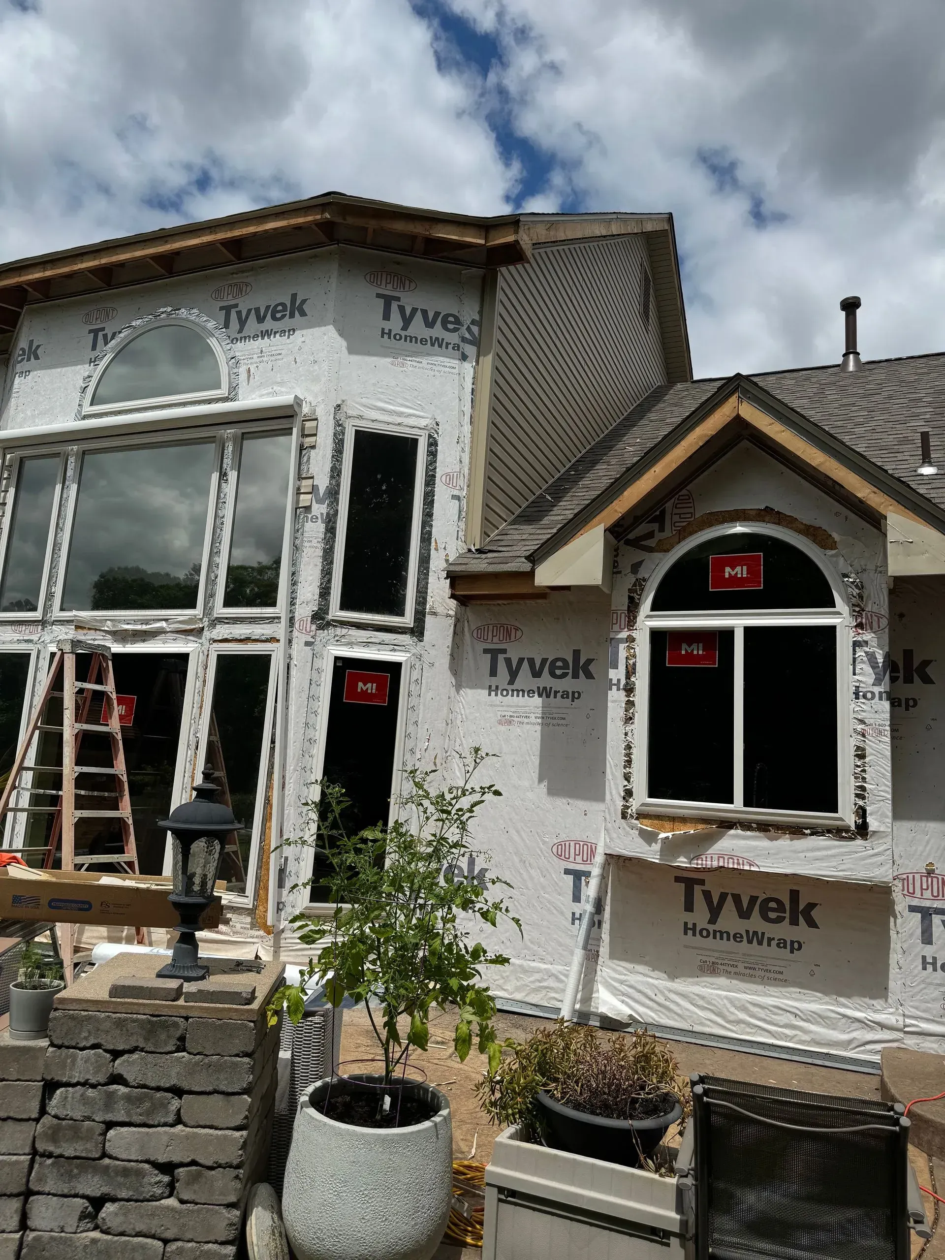 House under construction wrapped in Tyvek, with new windows and stone retaining wall in front
