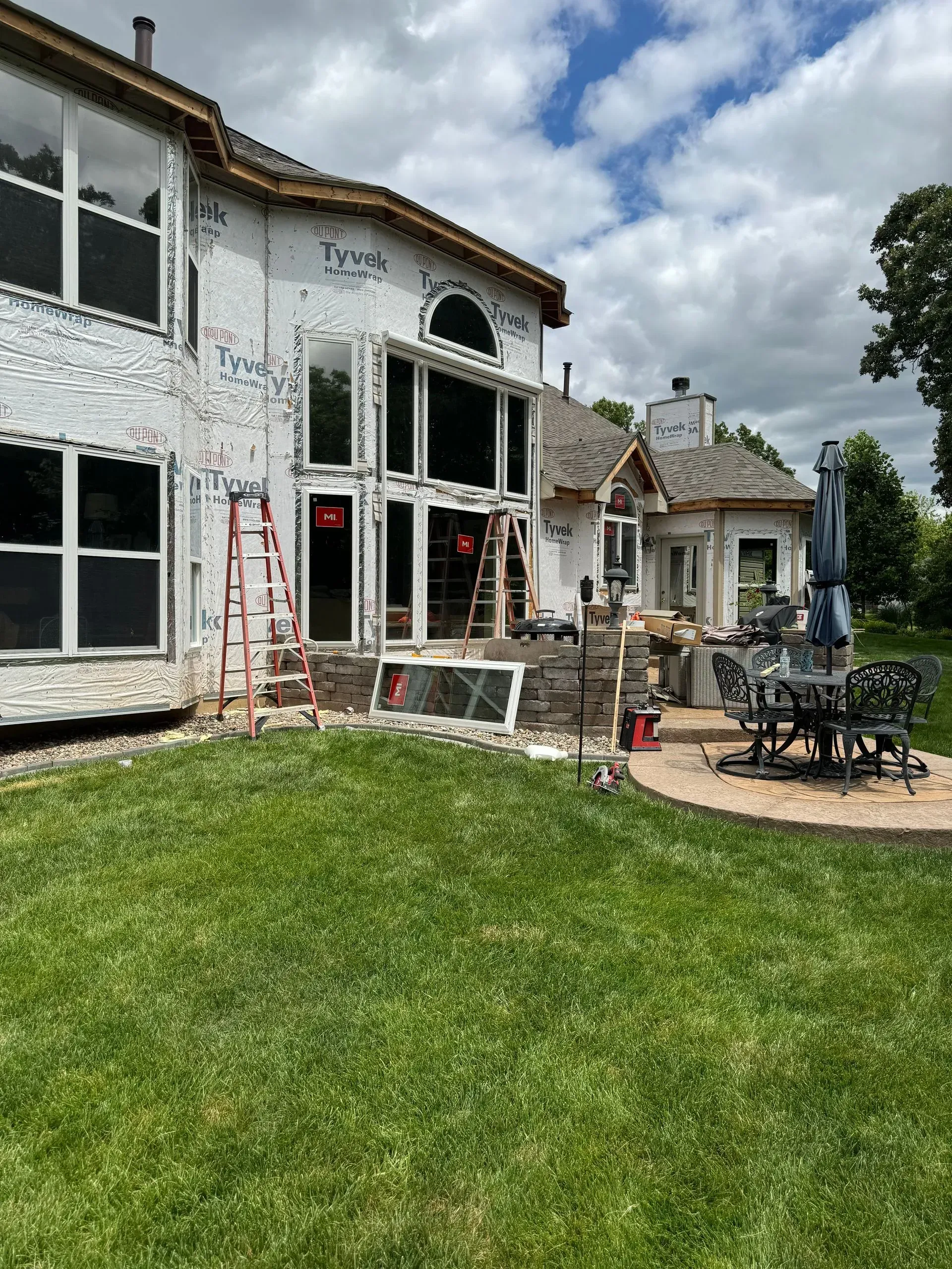 White two-story house with patio furniture and a grassy backyard under a cloudy sky