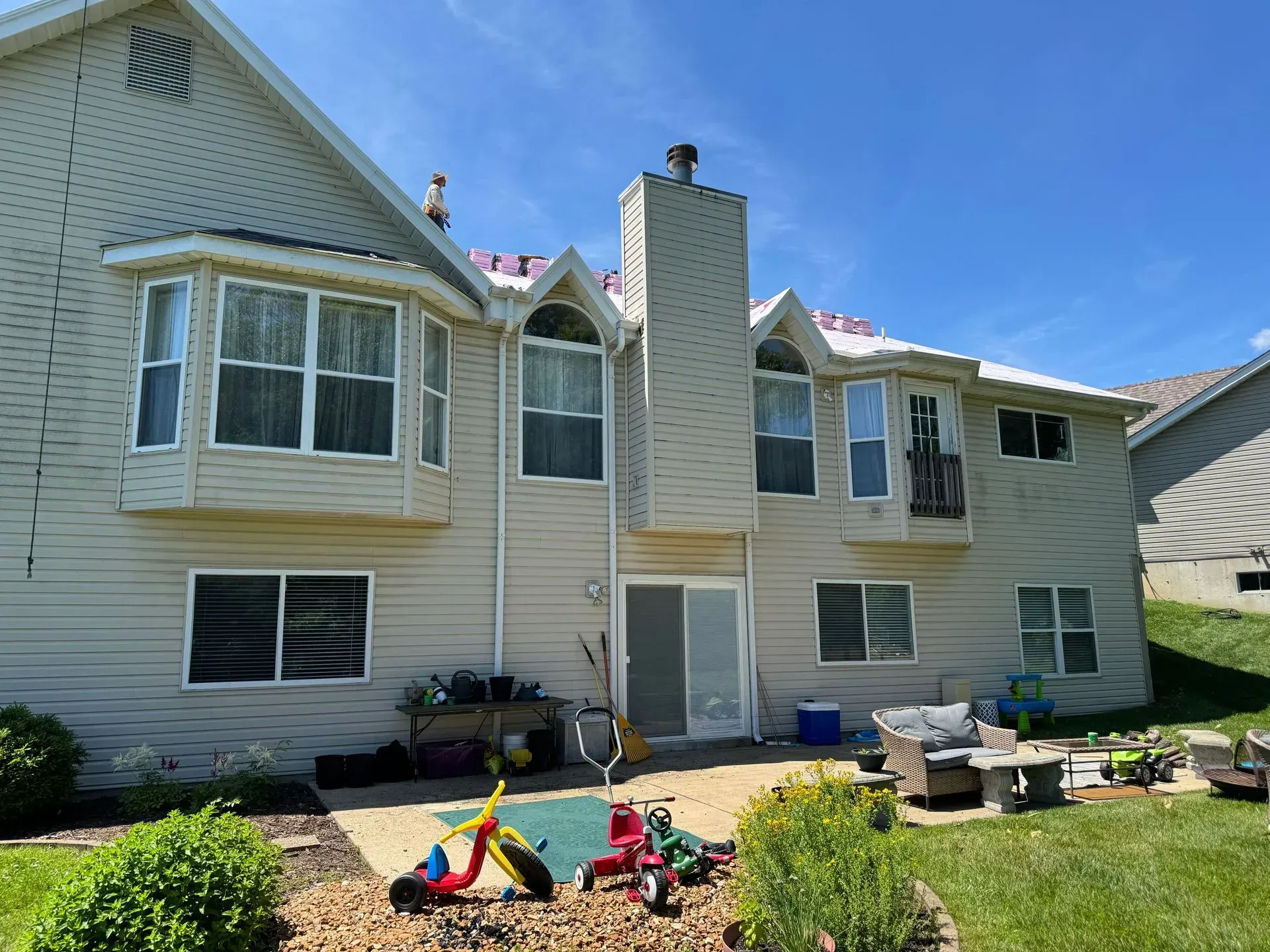 Backyard with toys and patio furniture behind a beige two-story house under a blue sky