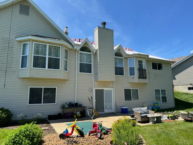 Backyard with toys and patio furniture behind a beige two-story house under a blue sky