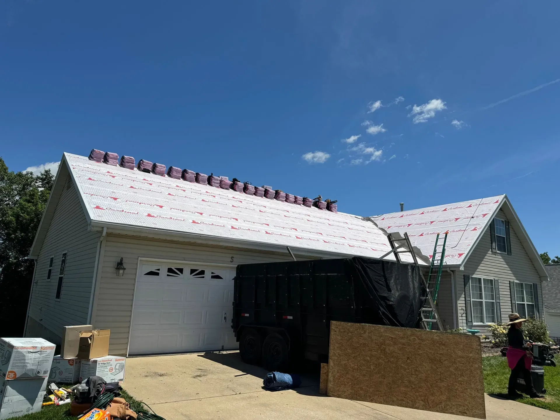 House under construction with white siding, roof work in progress, and workers on site under a blue sky