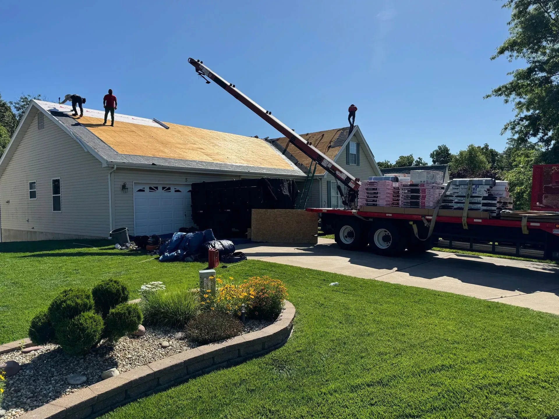 Workers repairing a white house roof with a crane truck in a suburban yard