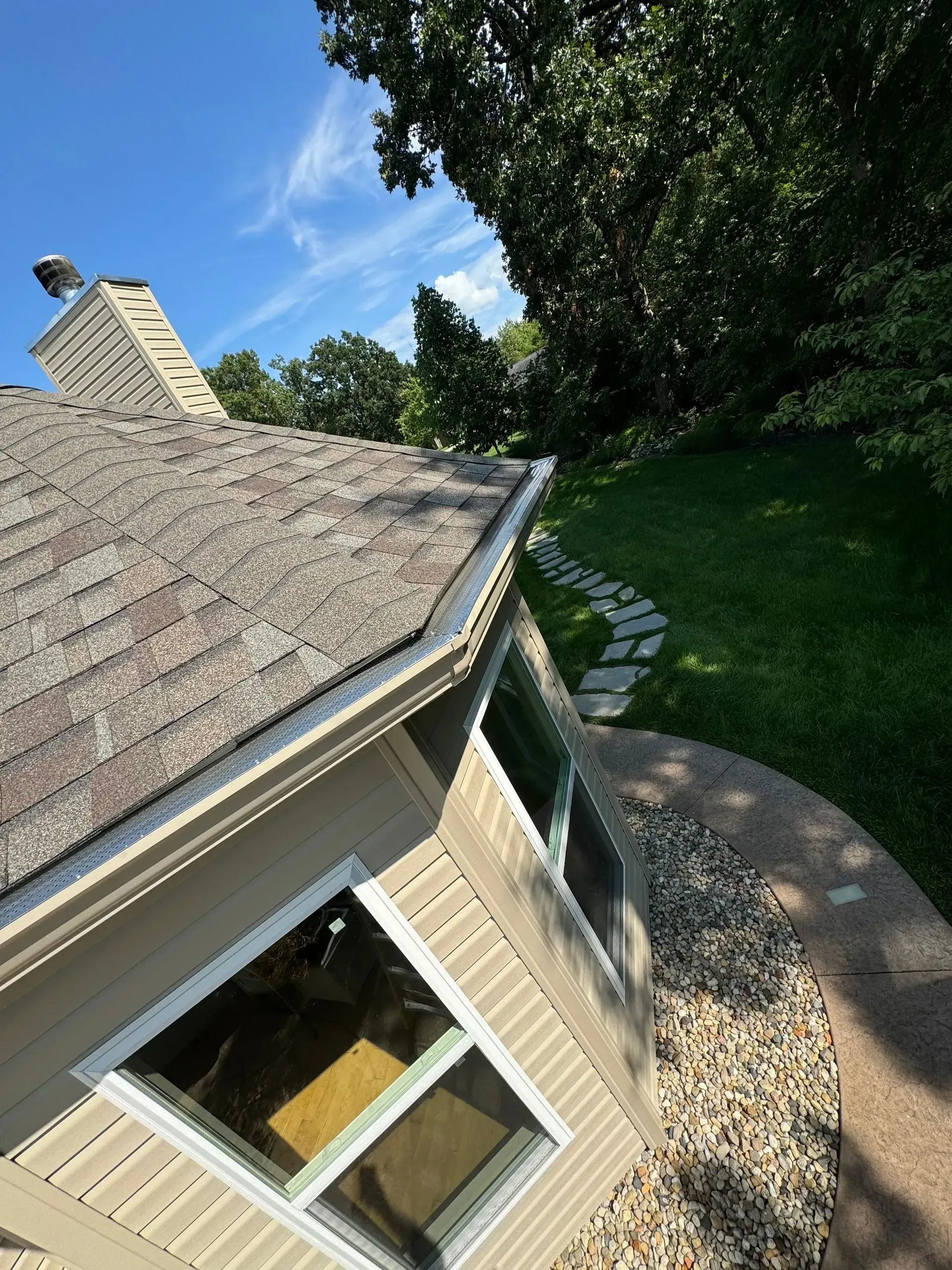 Tilted view of a house roof, window, and shaded lawn on a sunny day