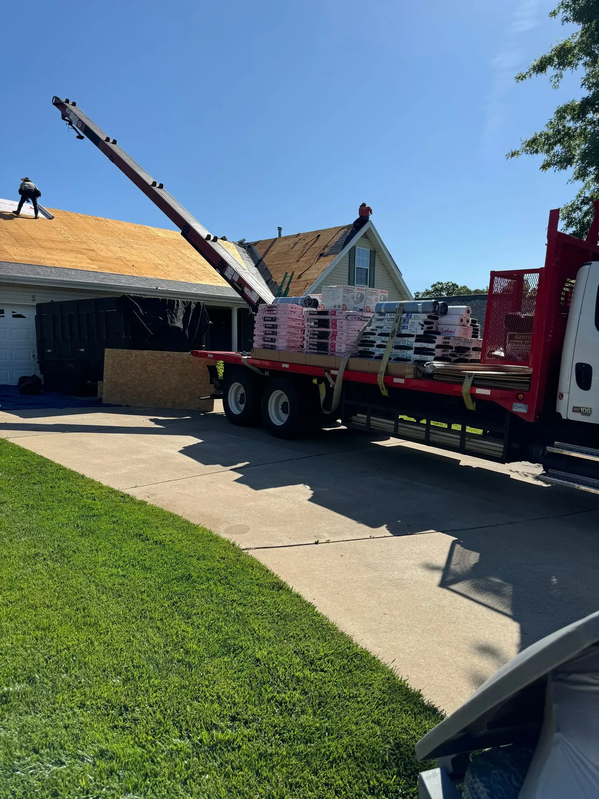 Fire truck ladder extended beside a house with a damaged roof in a sunny driveway