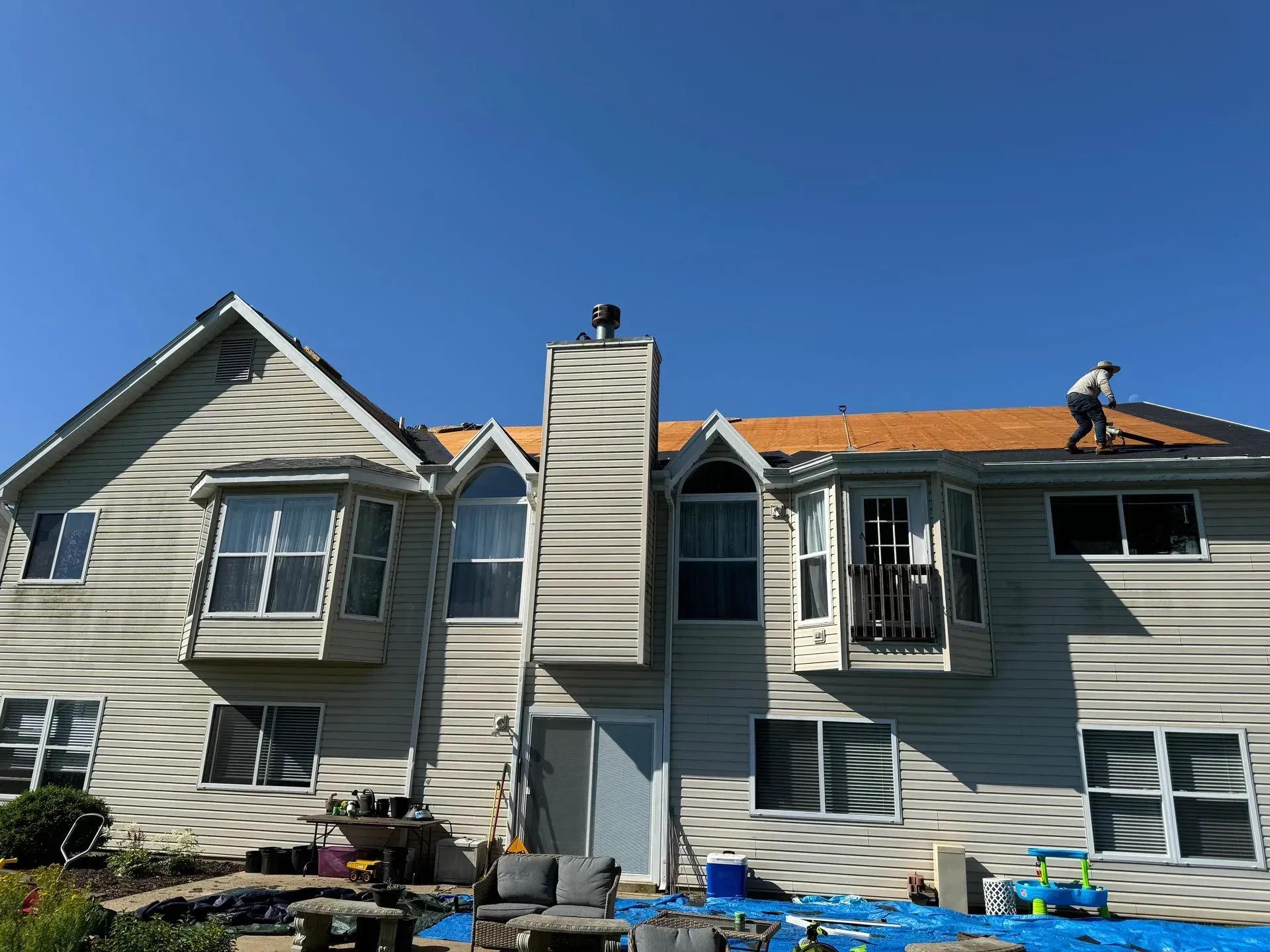 Workers repairing a house roof and siding under a clear blue sky