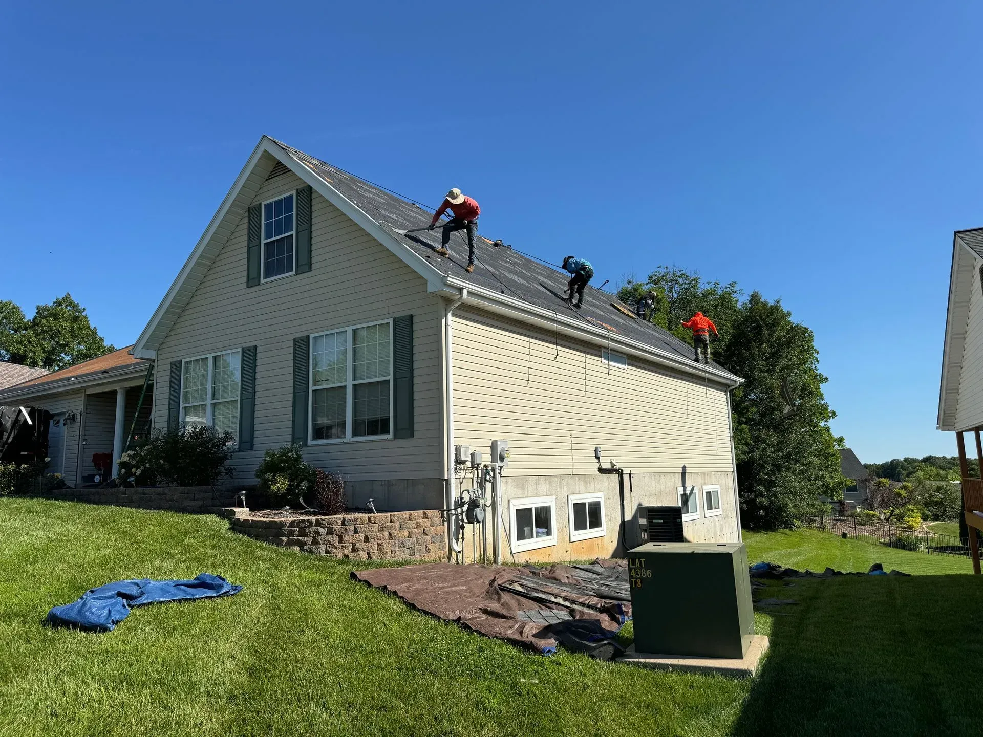 Workers repairing a house roof on a sunny day, with a ladder and debris on the lawn