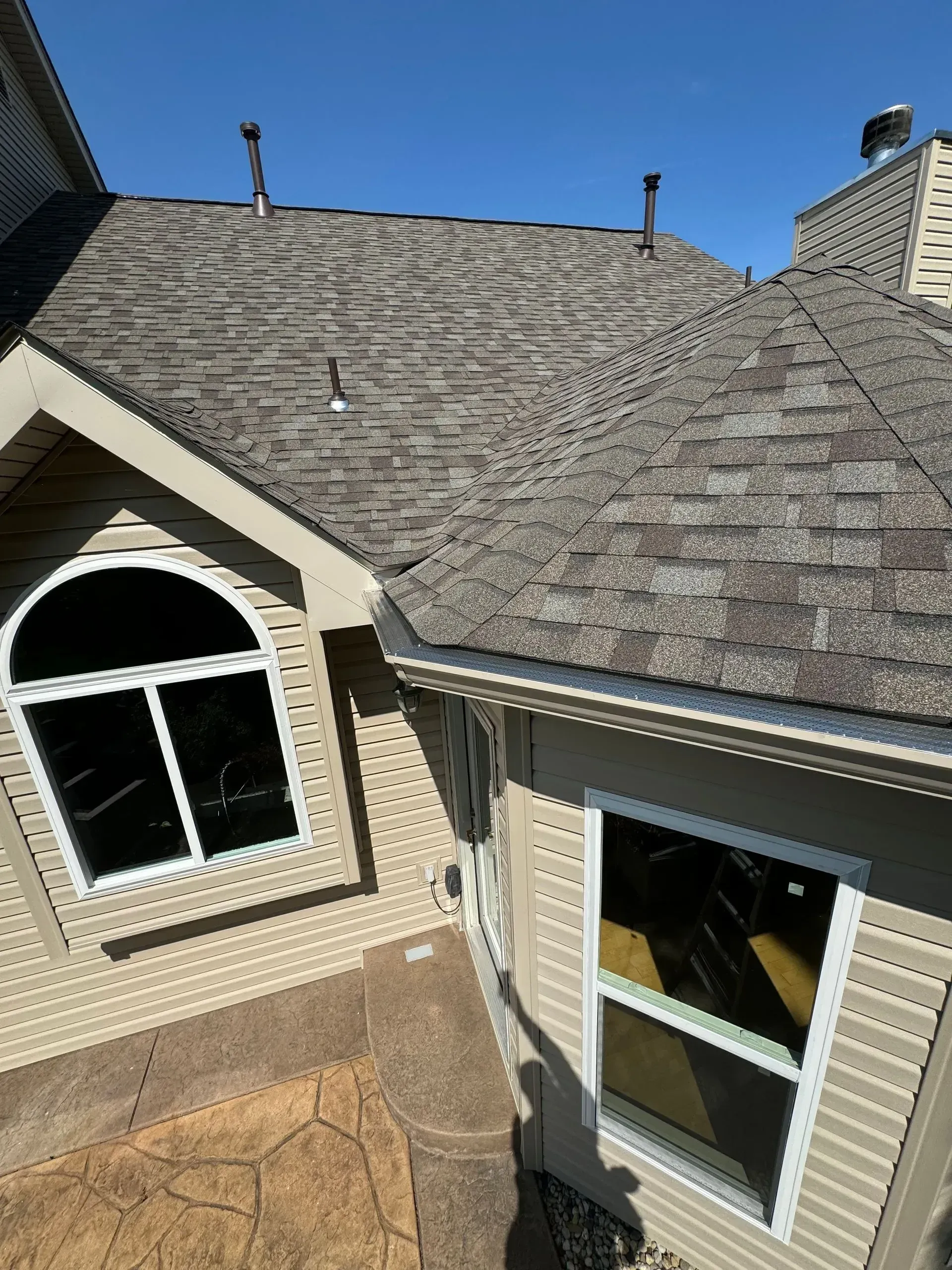 House roof with gray shingles and beige siding, seen from above under a clear blue sky