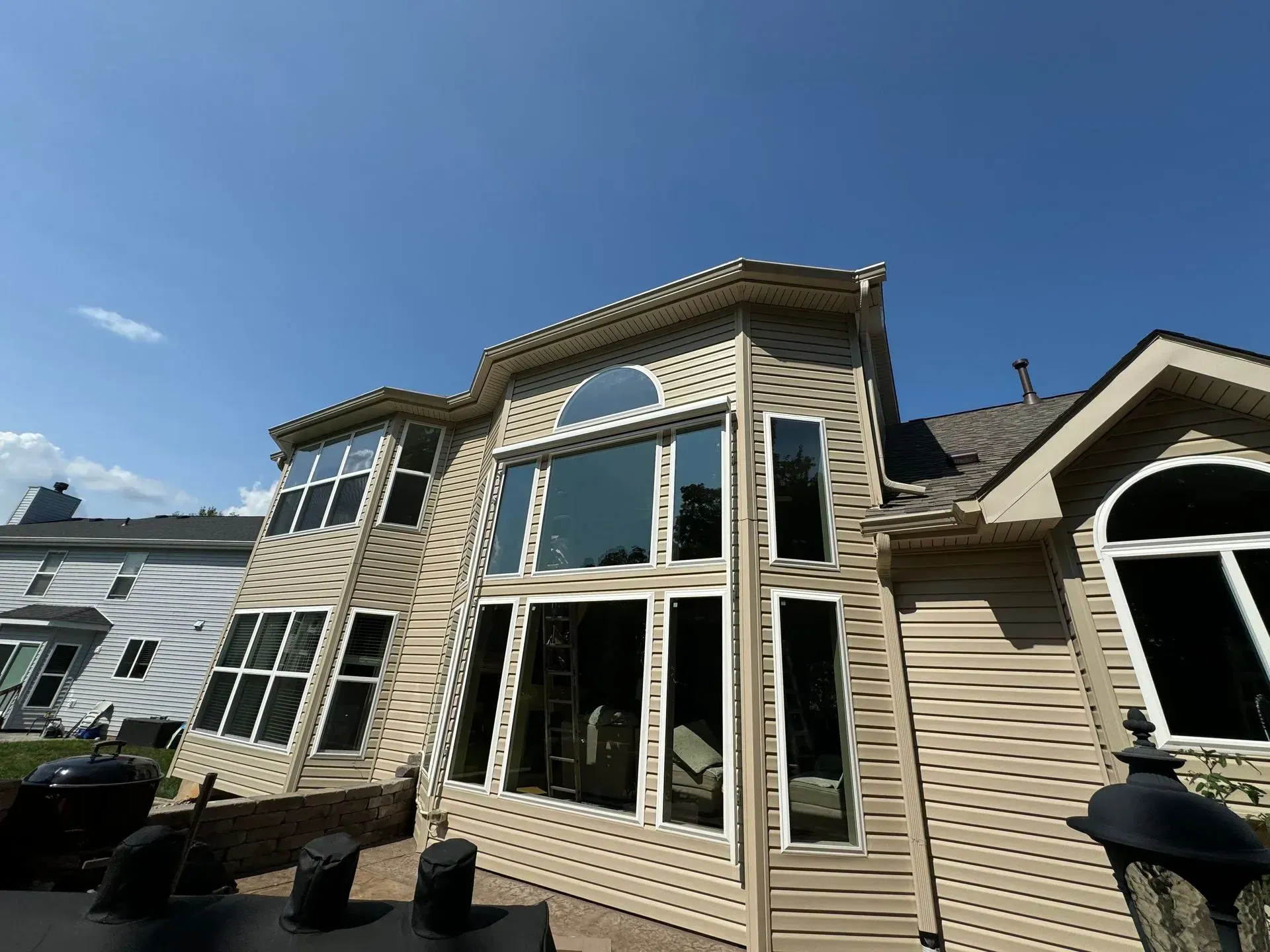Backyard view of a beige house with large windows and a blue sky
