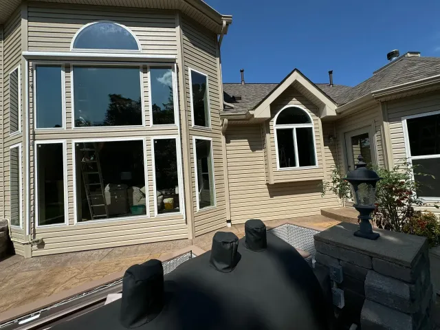 Stone house patio with large bay window, arched doorway, and outdoor grill in the foreground