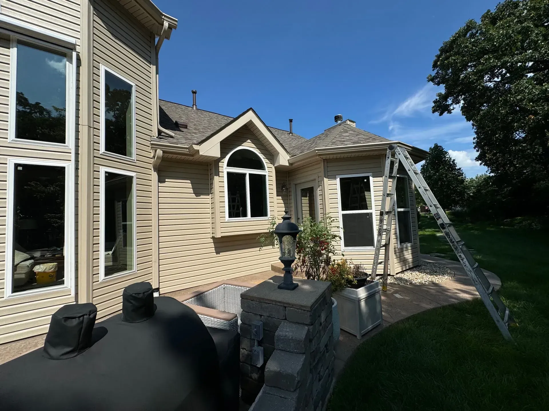 Exterior of a beige house with a backyard deck, ladder, and sunny blue sky