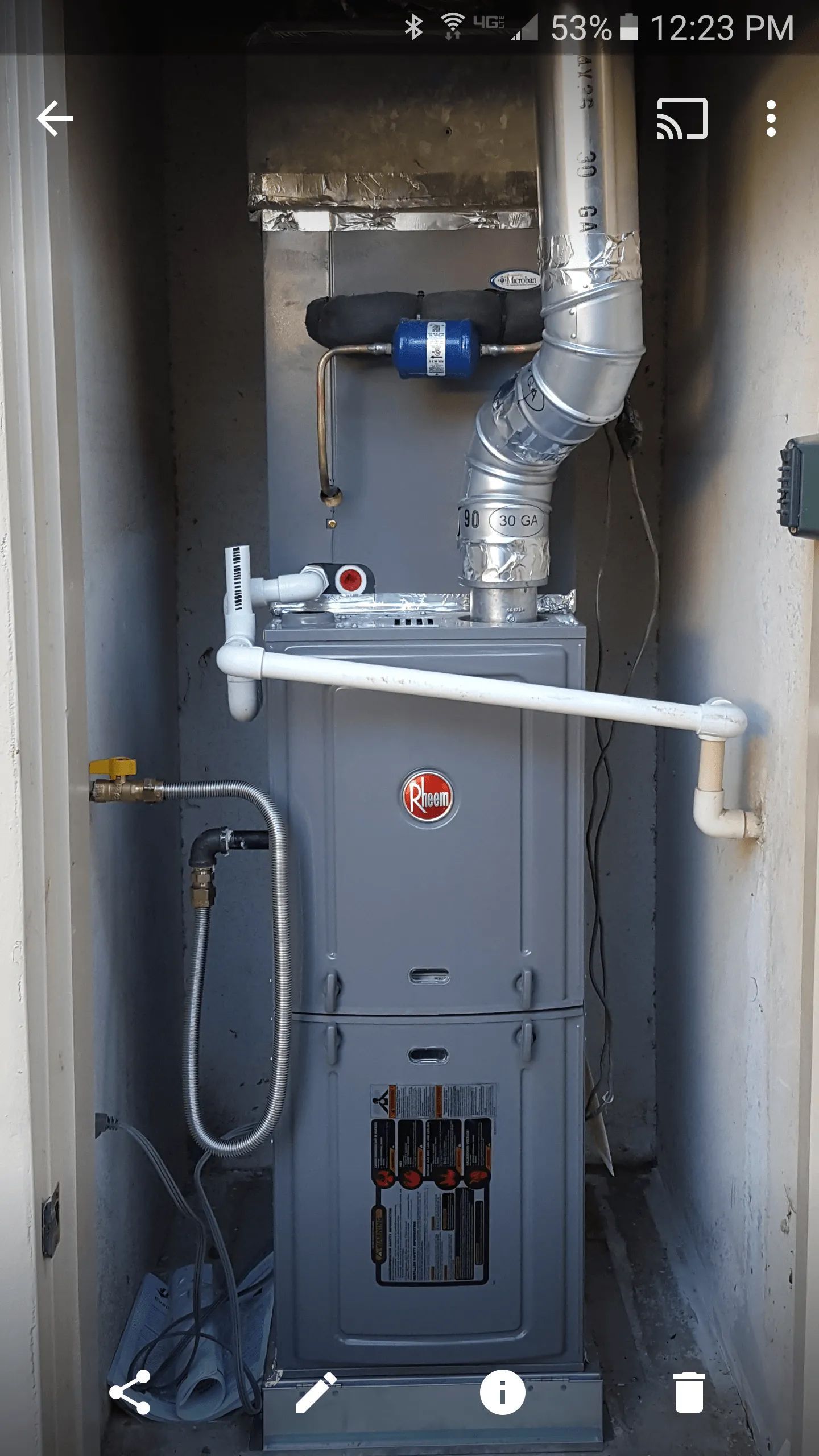 Gray Rheem furnace with metal flue pipe in an outdoor enclosure.