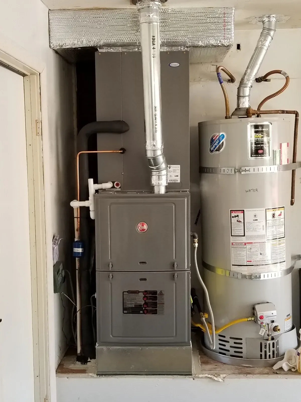 Gray HVAC unit and water heater in a utility closet with ductwork and copper piping.
