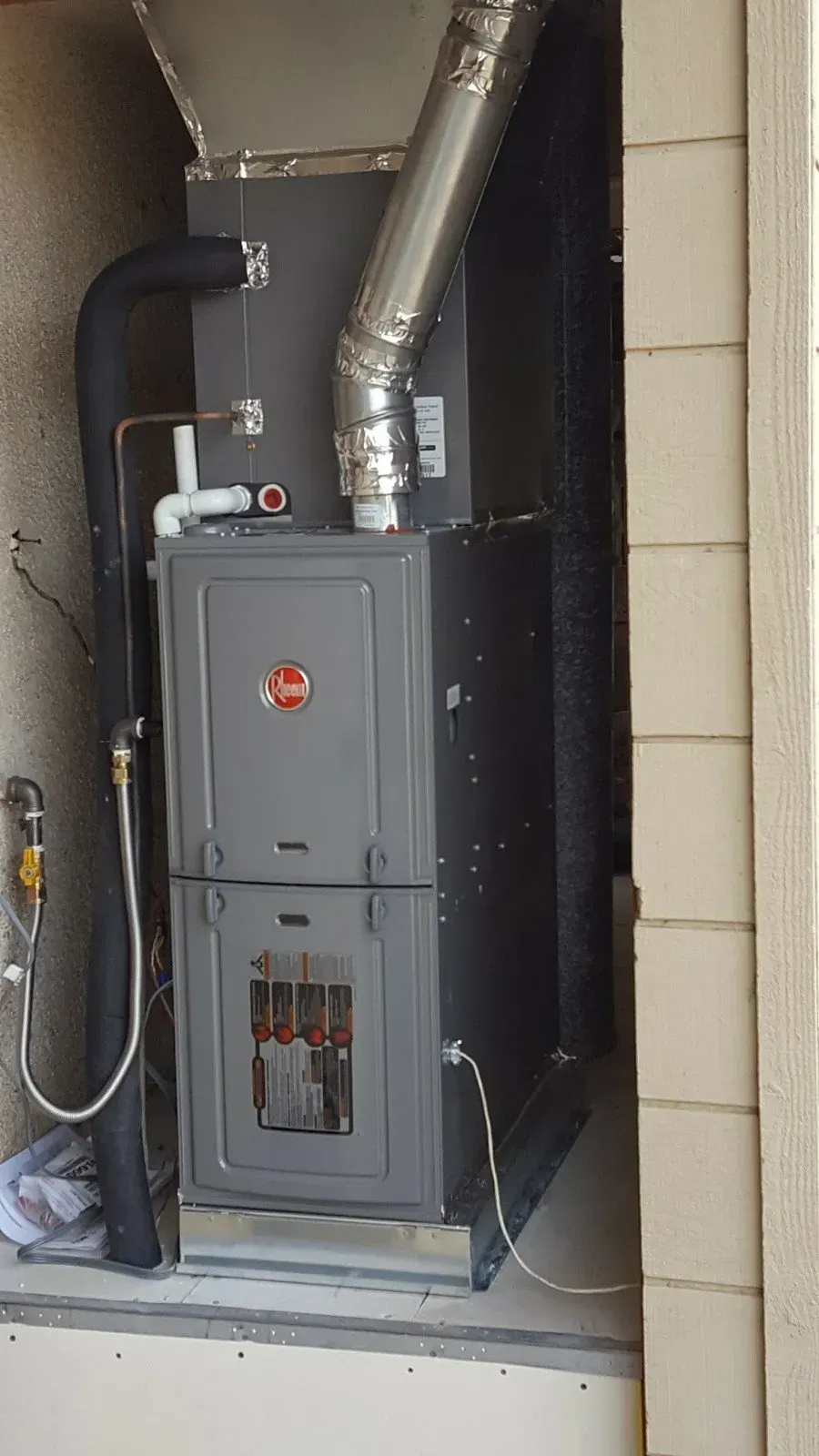 Rheem furnace unit inside a recessed wall. Silver chimney, black ductwork, and gray cabinet.
