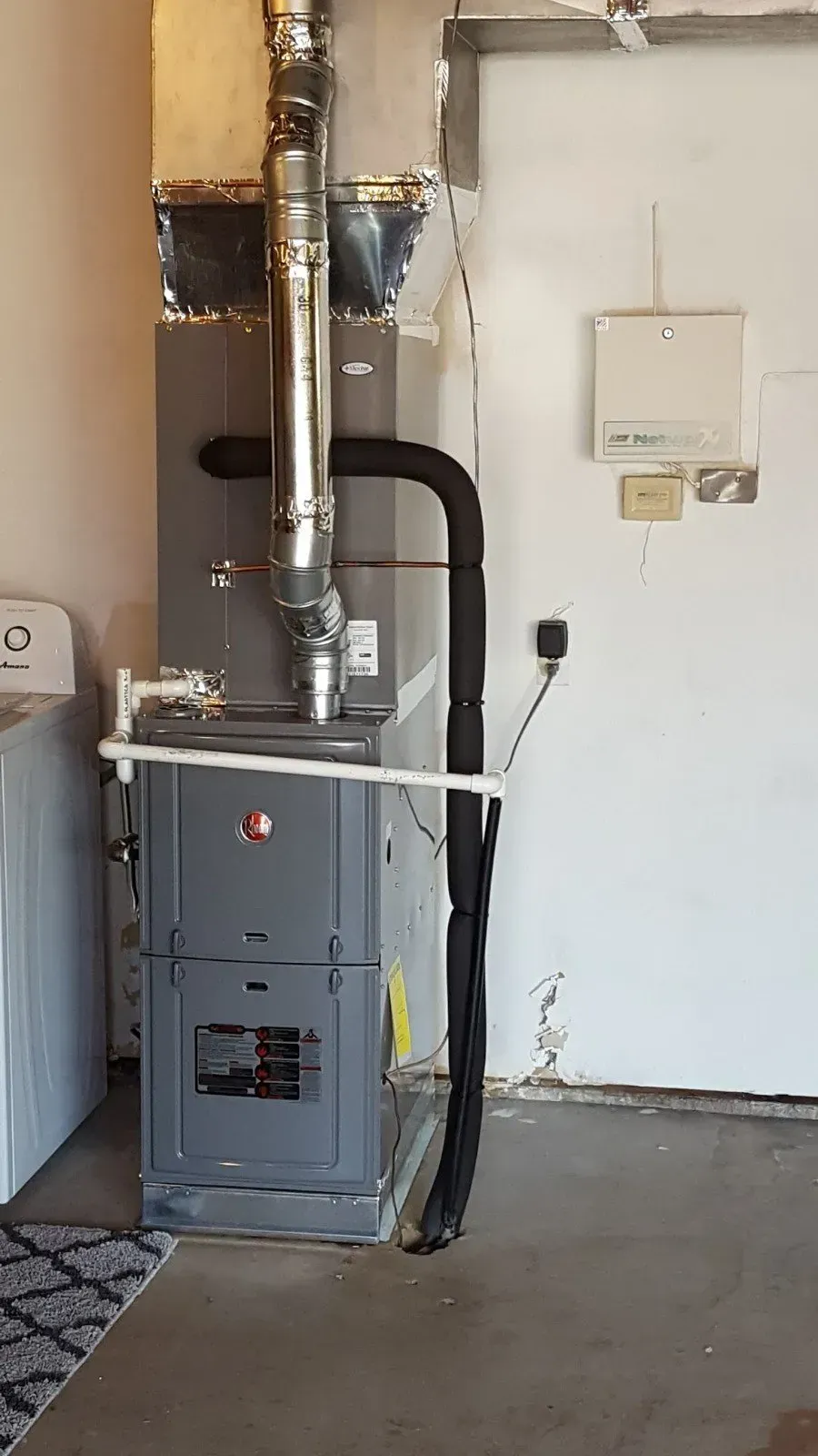 Furnace in a garage with ventilation ducts and electrical connections along a wall.