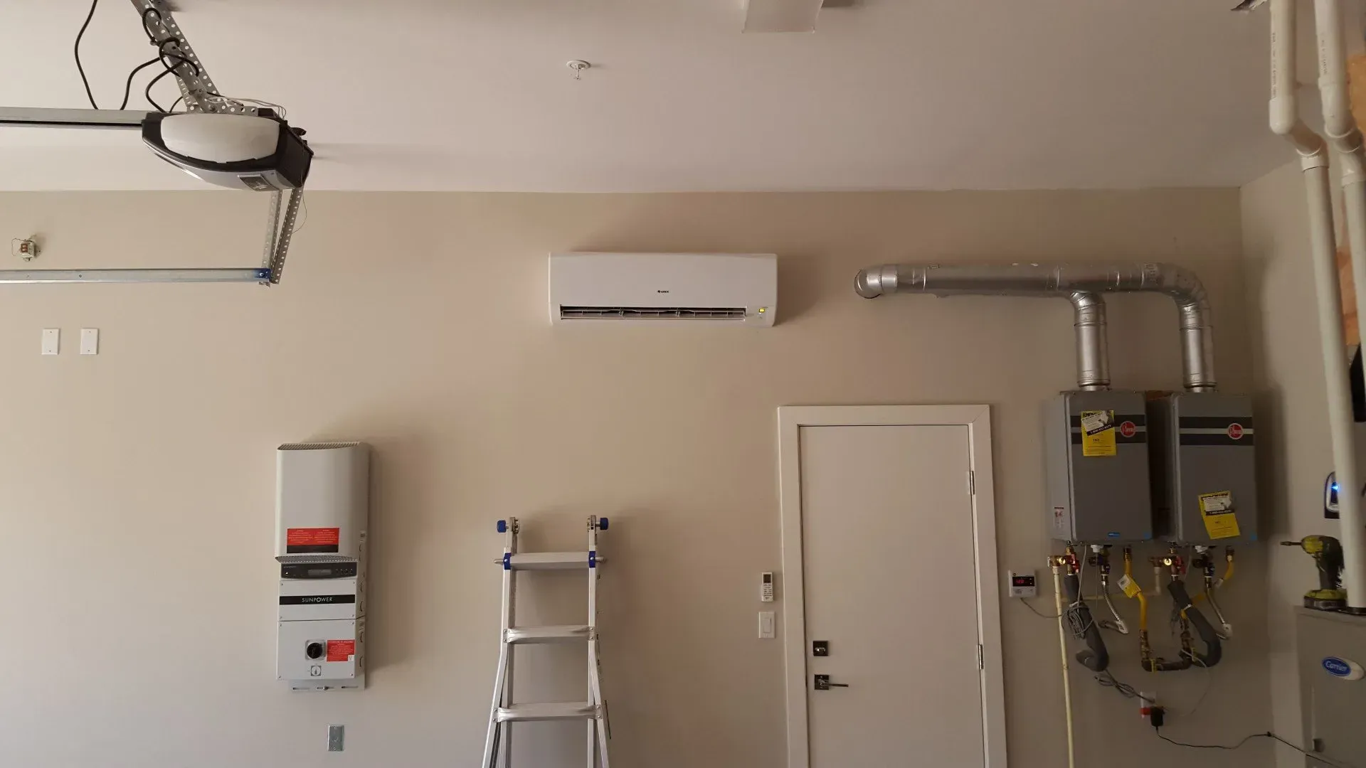 Garage interior with an air conditioner, door, water heaters, and garage door opener.