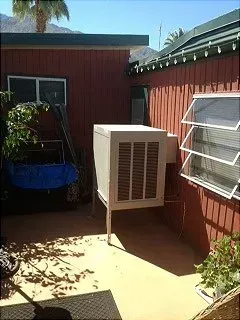 An outdoor air cooler attached to a red building with open windows and shadows.