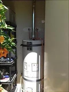 Water heater in a small, outdoor enclosure with a vent pipe; copper pipes visible.