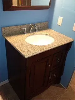 Bathroom vanity with granite countertop, oval sink, and dark wood cabinet against blue wall.