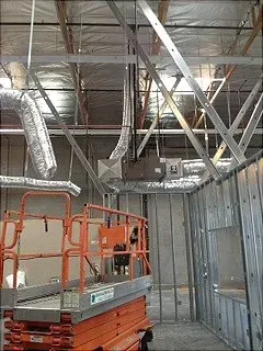 Orange scissor lift inside a building under construction, near HVAC equipment and metal studs.