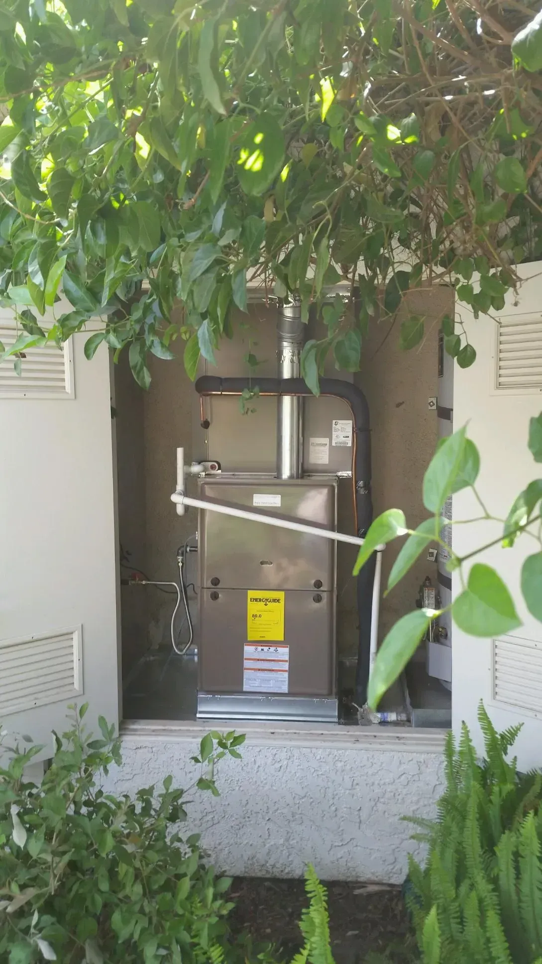 HVAC unit installed outdoors, encased in a concrete structure, partially obscured by green foliage.