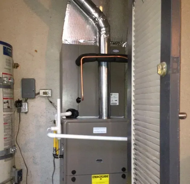 Furnace and water heater in a utility closet with vent pipe and gas lines.