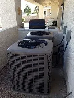 Two York air conditioning units in an outdoor alcove next to electrical boxes. A barbecue grill is in the background.