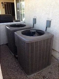 Two outdoor air conditioning units next to a light-colored wall.