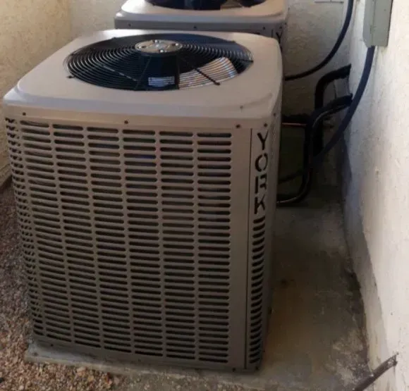 Two York brand air conditioning units outside, on a concrete pad, against a wall.