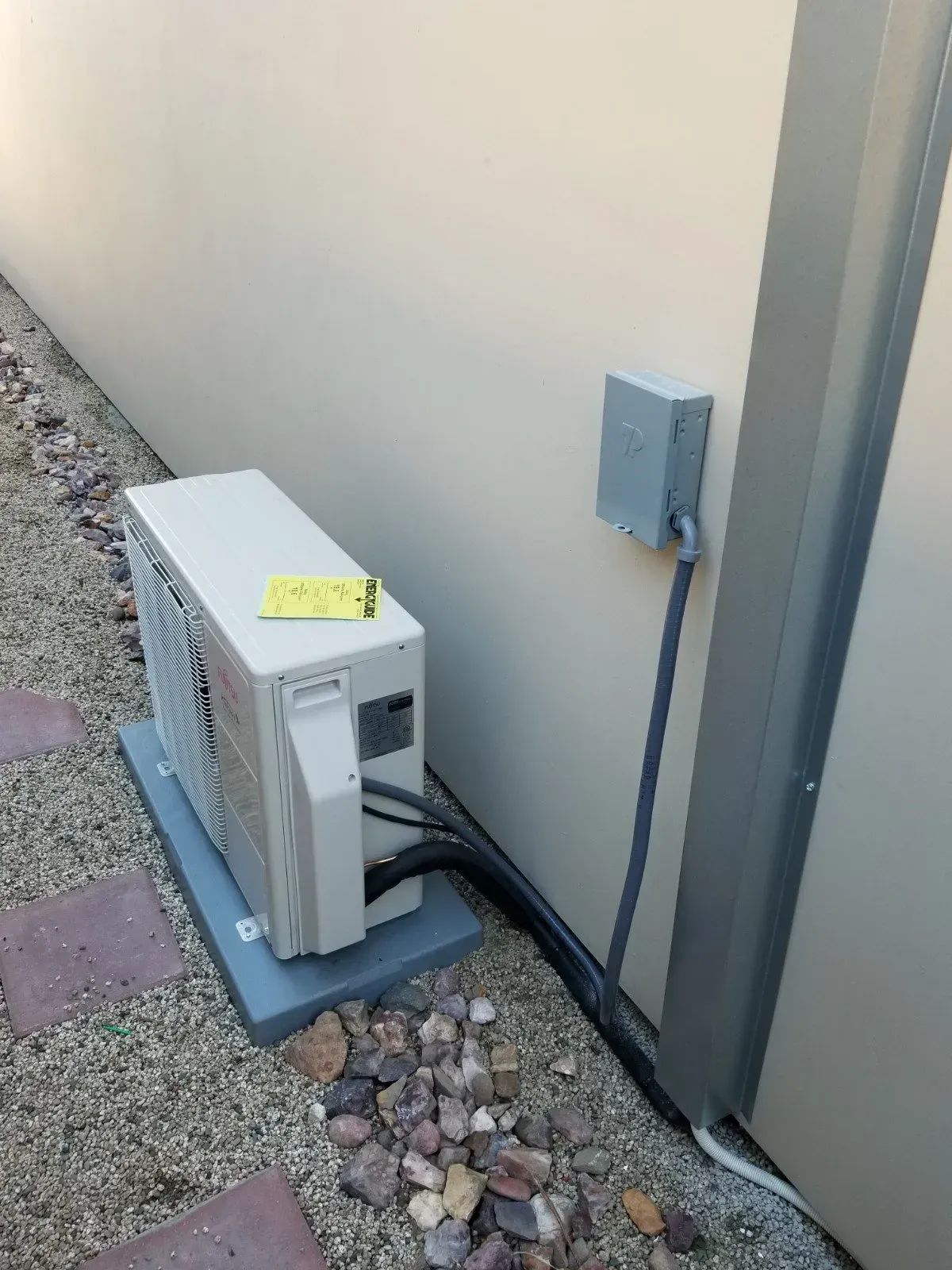 Air conditioning unit on a concrete pad next to a wall, connected to an electrical box.