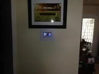 Wall with a framed green van photo and a white control panel below.