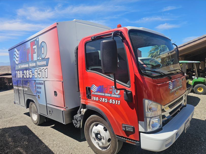Red and gray service truck with company logo parked outdoors on a sunny day.