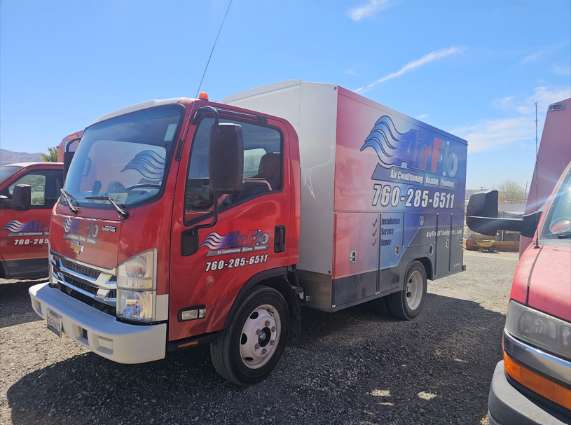 Red and white service truck with company logo parked outdoors on a sunny day.