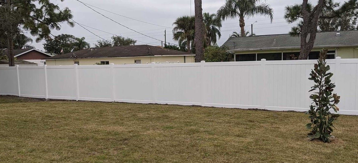 A white vinyl fence surrounds a grassy yard in front of a house.