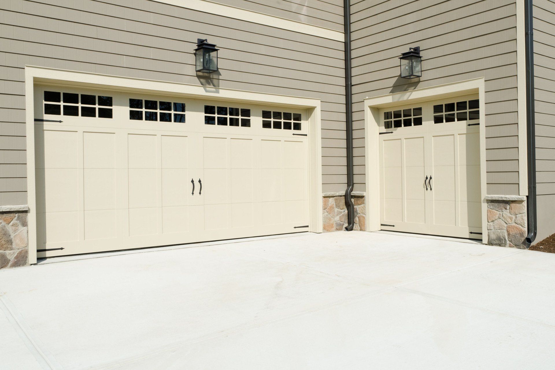 Beige garage doors with windows, flanked by sconces, in front of a gray-sided building.