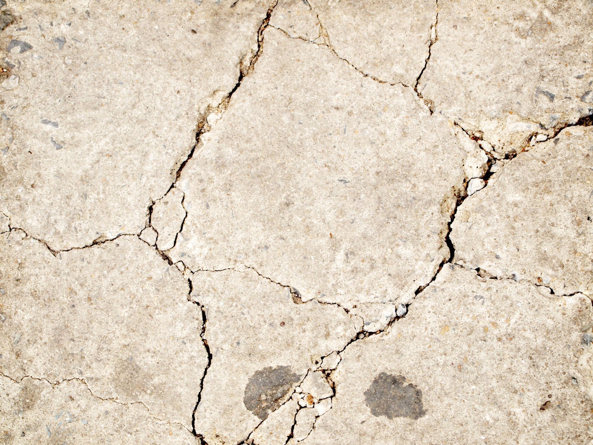 Cracked concrete surface with several large fissures, showing wear and discoloration.
