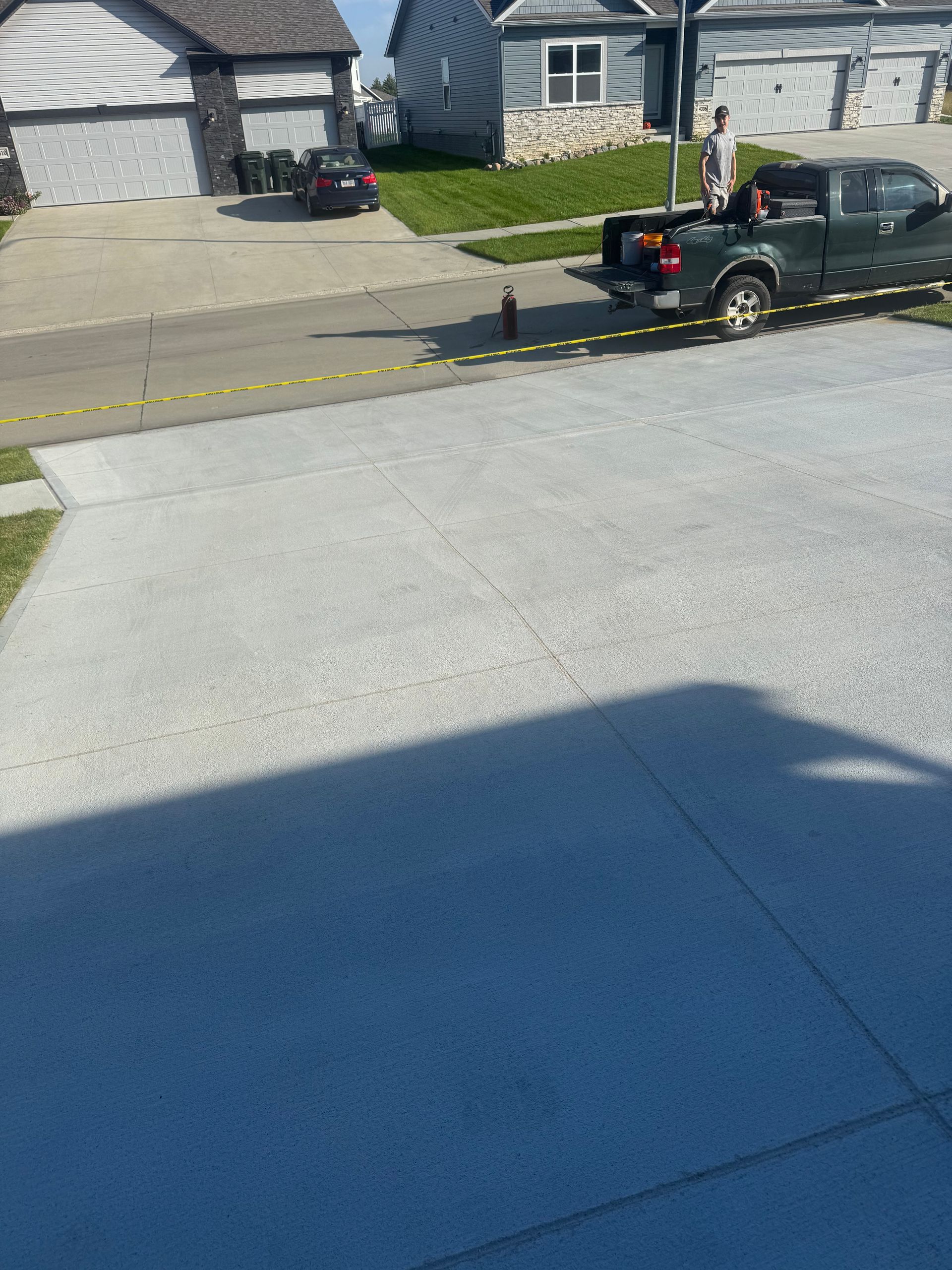 Person unloading items from a green pickup truck parked on a driveway. Houses and a street are in the background.