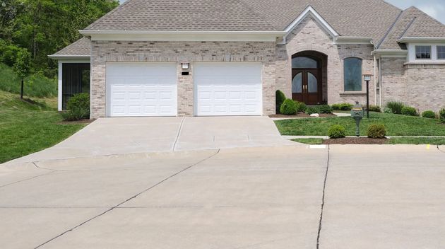Tan brick house with two white garage doors and concrete driveway.