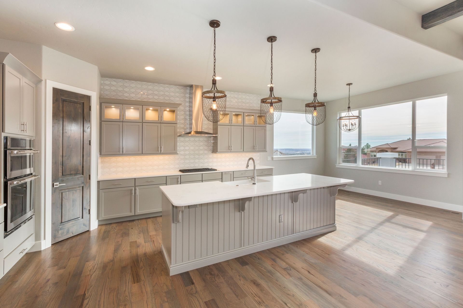Spacious kitchen with gray cabinets, large island, pendant lights, and hardwood floors.