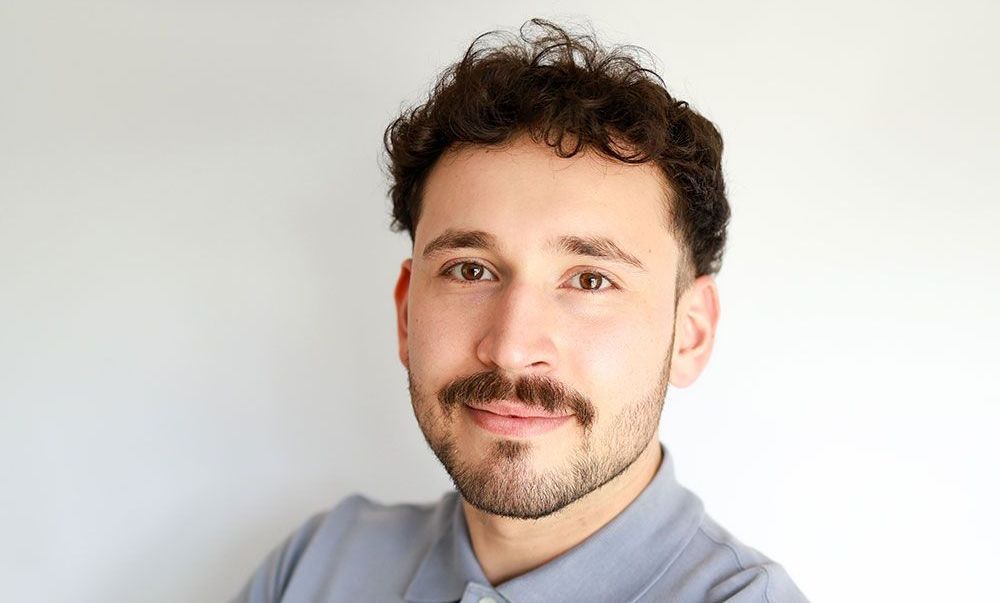 A man with a beard and mustache is standing with his arms crossed.