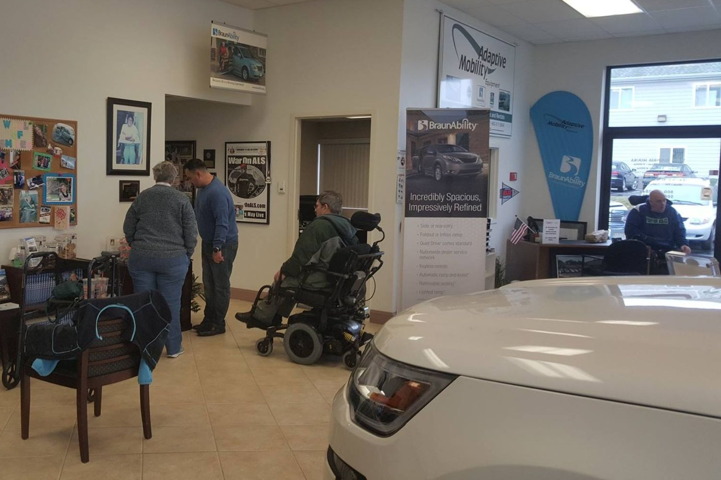 Interior of a business with people, including a person in a wheelchair, and a white car.