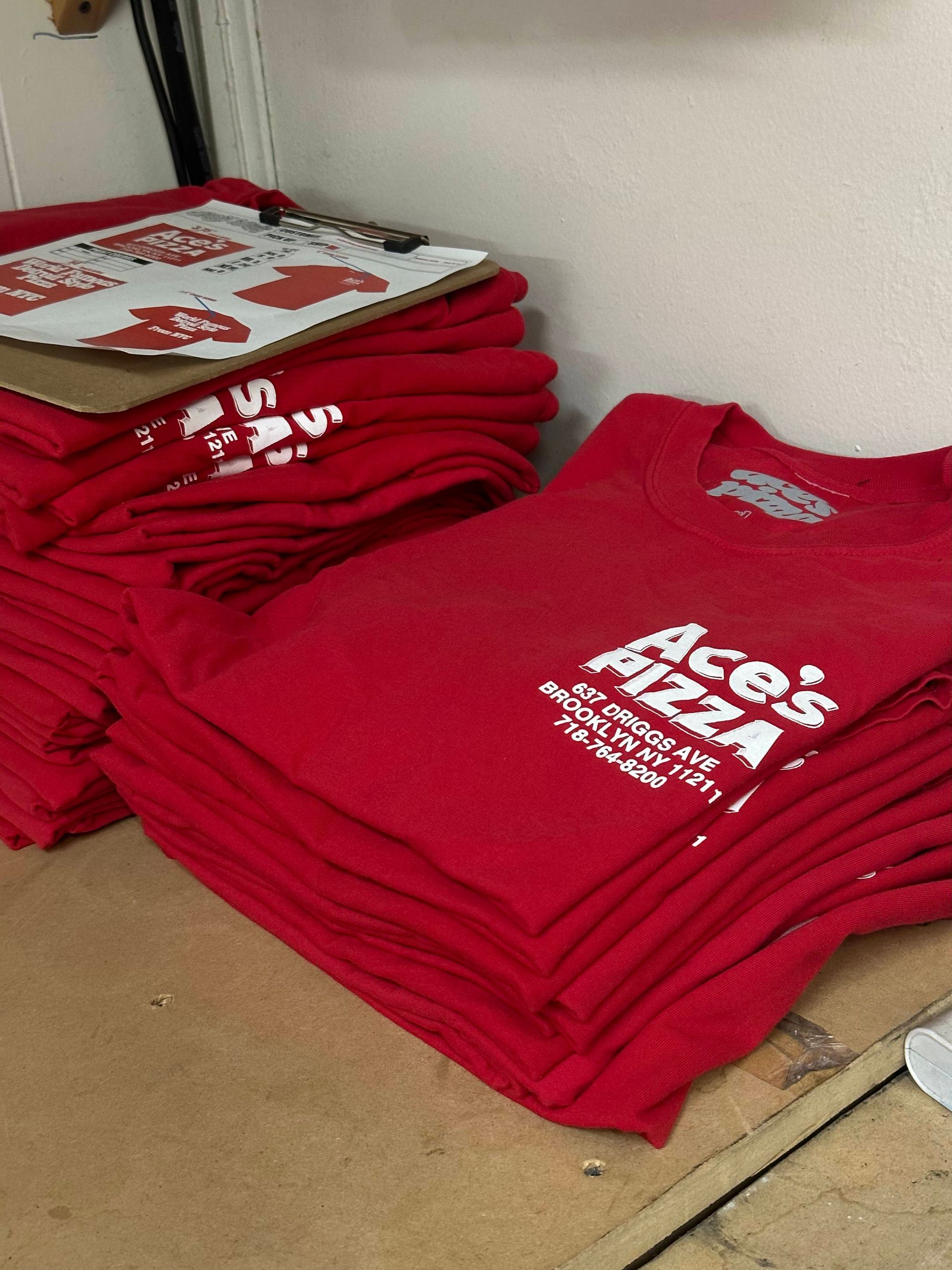 a stack of red ace's pizza t-shirts