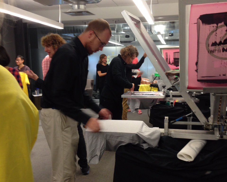 a man in a black shirt is standing in front of a screen printing machine