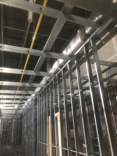 A building under construction with metal frames and pipes hanging from the ceiling.