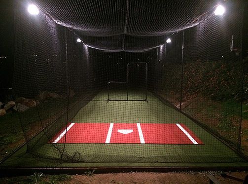A baseball field with a batting cage in the background at night.