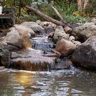 There is a small waterfall in the middle of a pond surrounded by rocks.