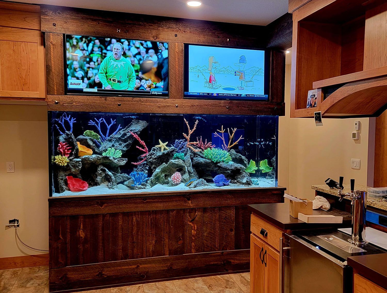 A large aquarium is sitting in a kitchen next to two televisions.