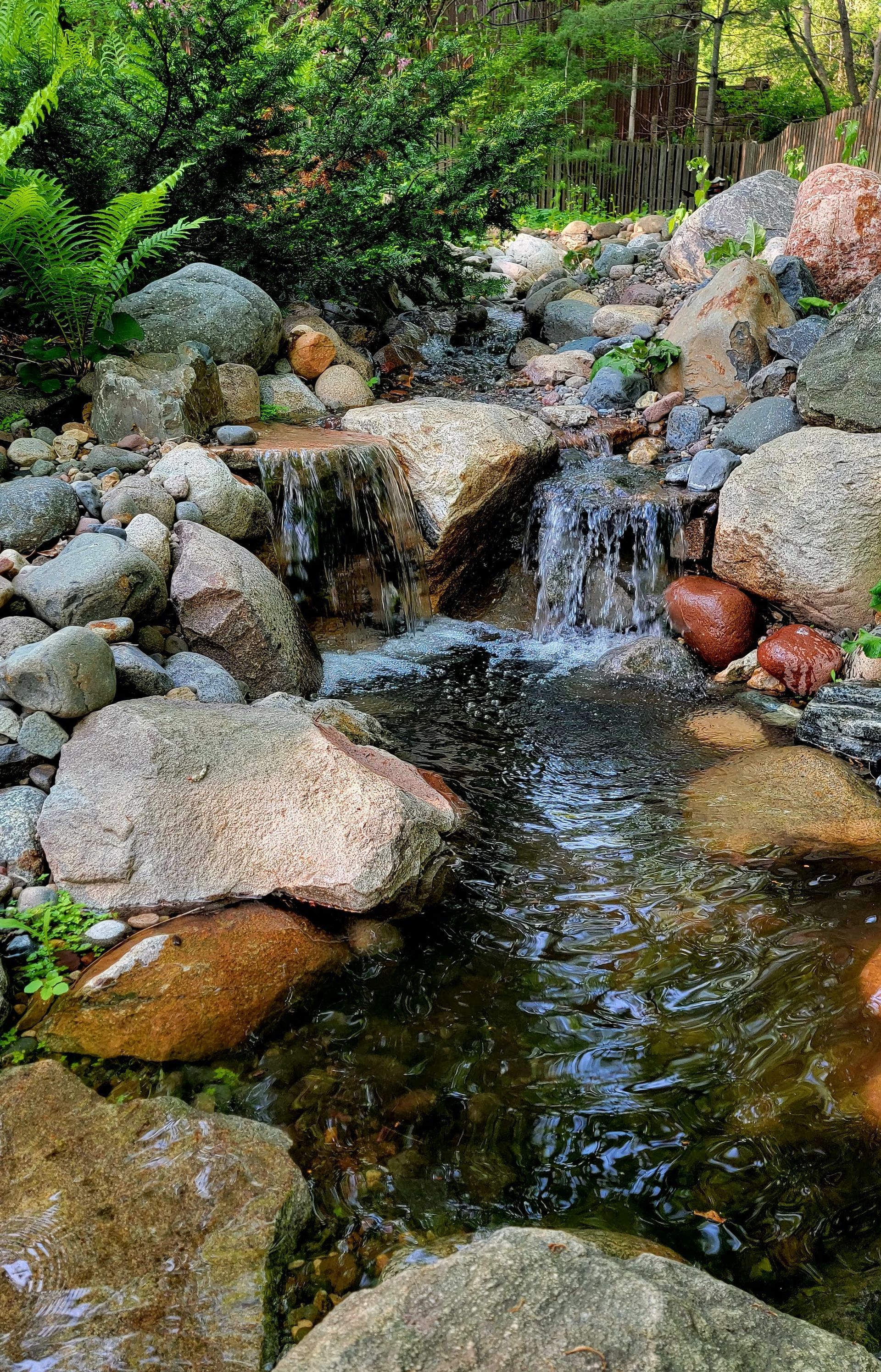 A small waterfall surrounded by rocks and trees in a garden.