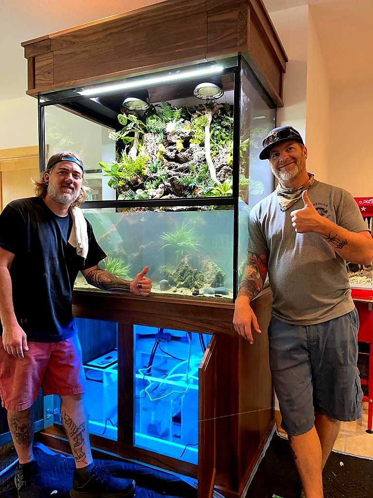 Two men are standing in front of a large fish tank.
