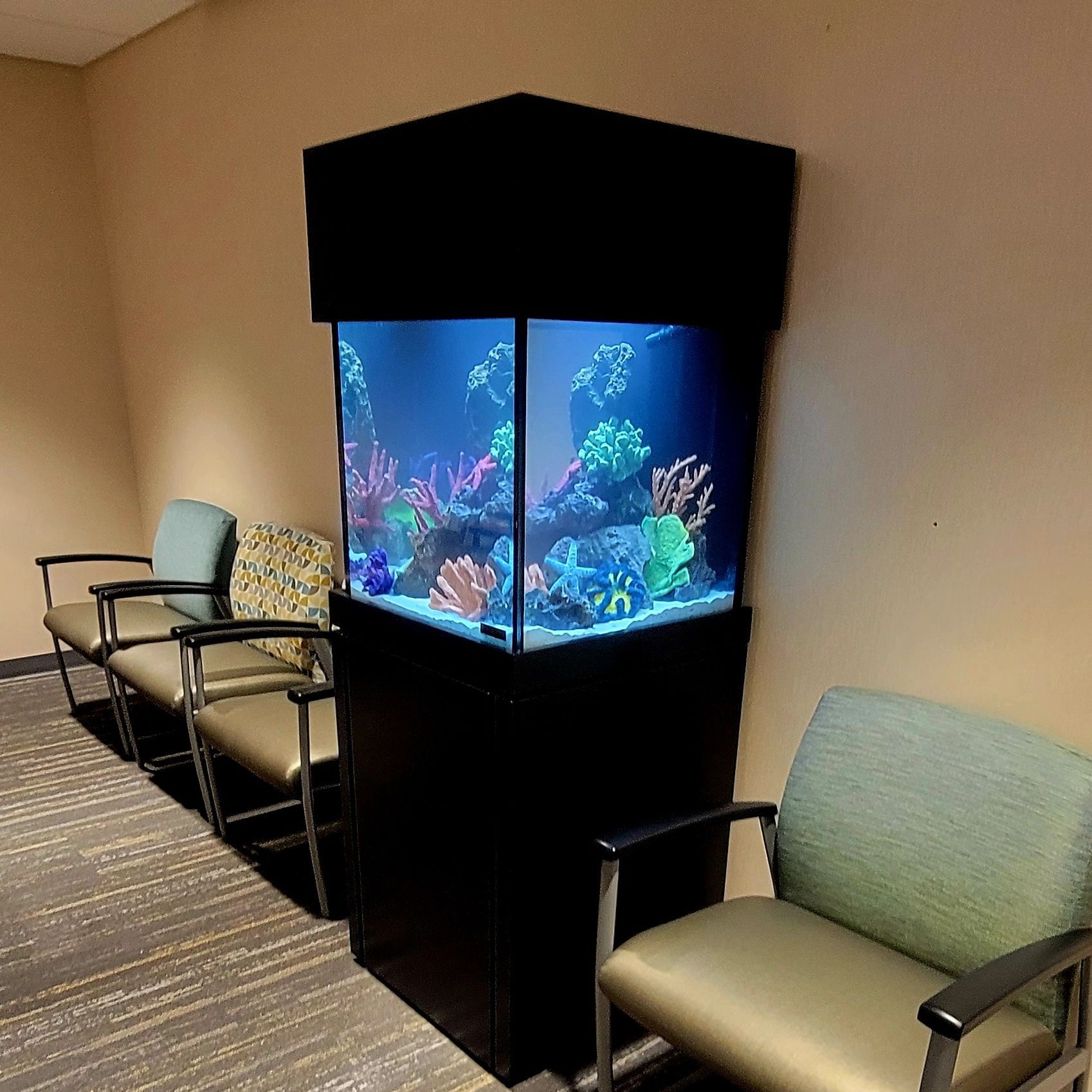 A large aquarium is sitting in a waiting room next to chairs.